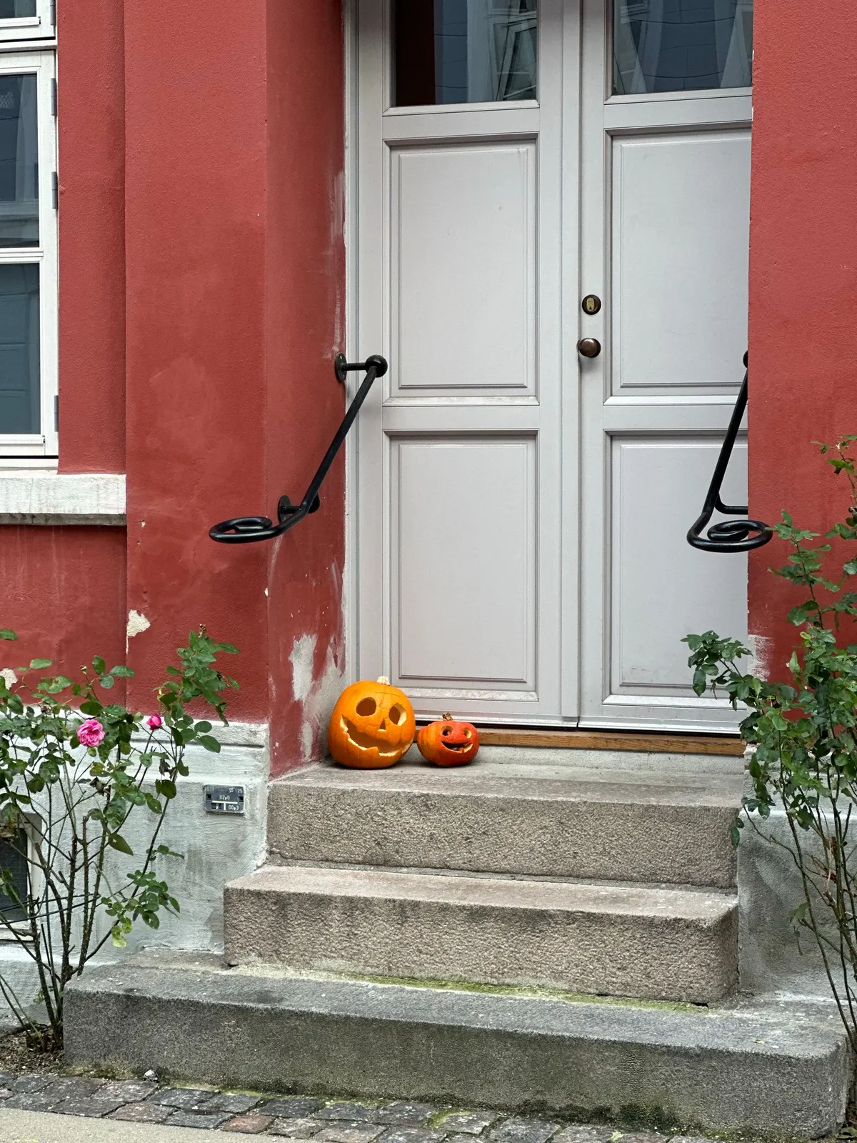 A large and a small carved jack-o'-lantern on gray stone steps in front of a pale double door