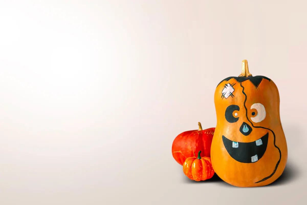 Tall orange gourd painted with a stitched monster face, flat-top hair and a bandage, beside two small pumpkins