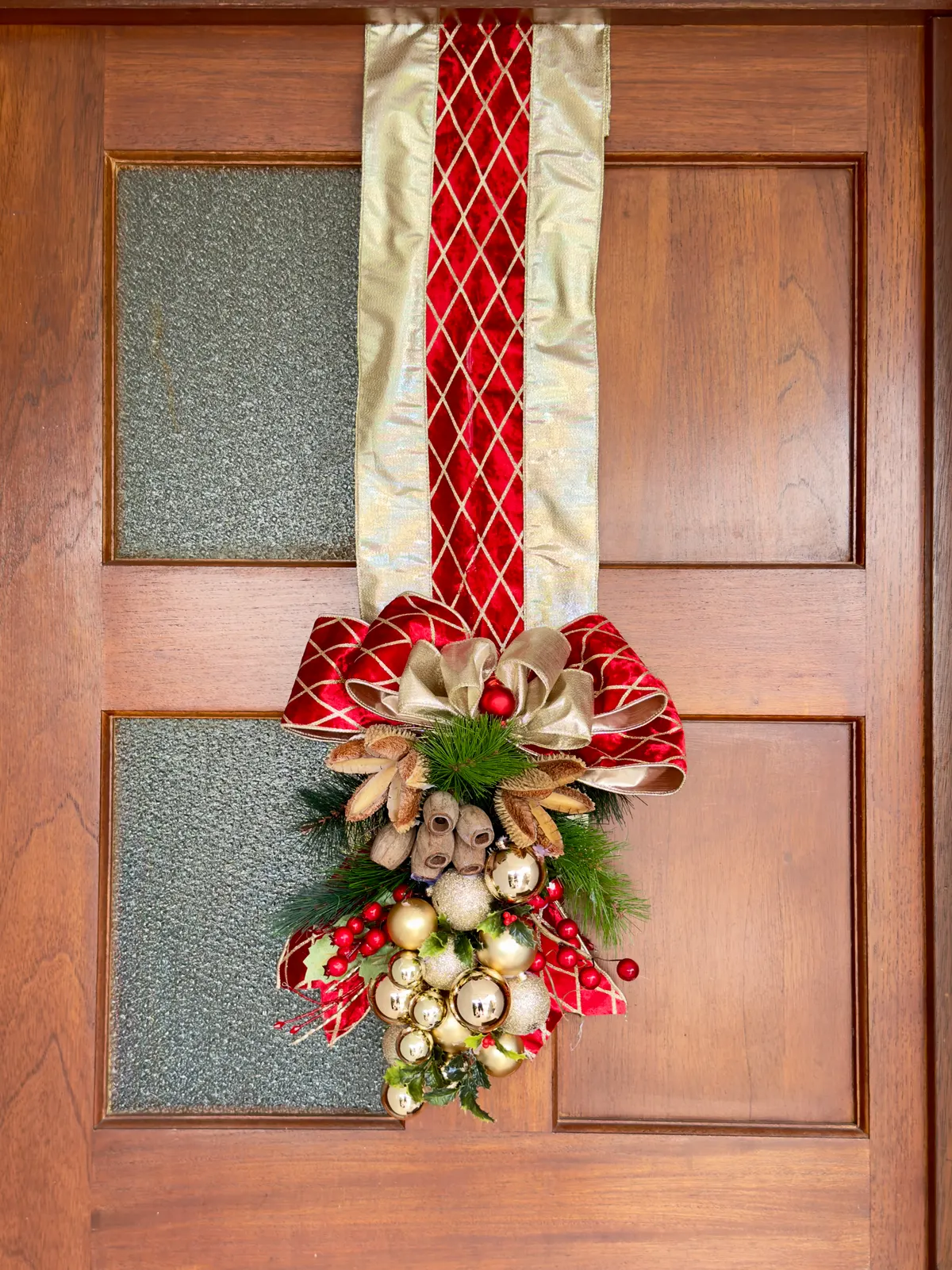Wooden glass-paneled door with a long red and gold ribbon swag, big bow, pine sprigs, pinecones and jingle bells