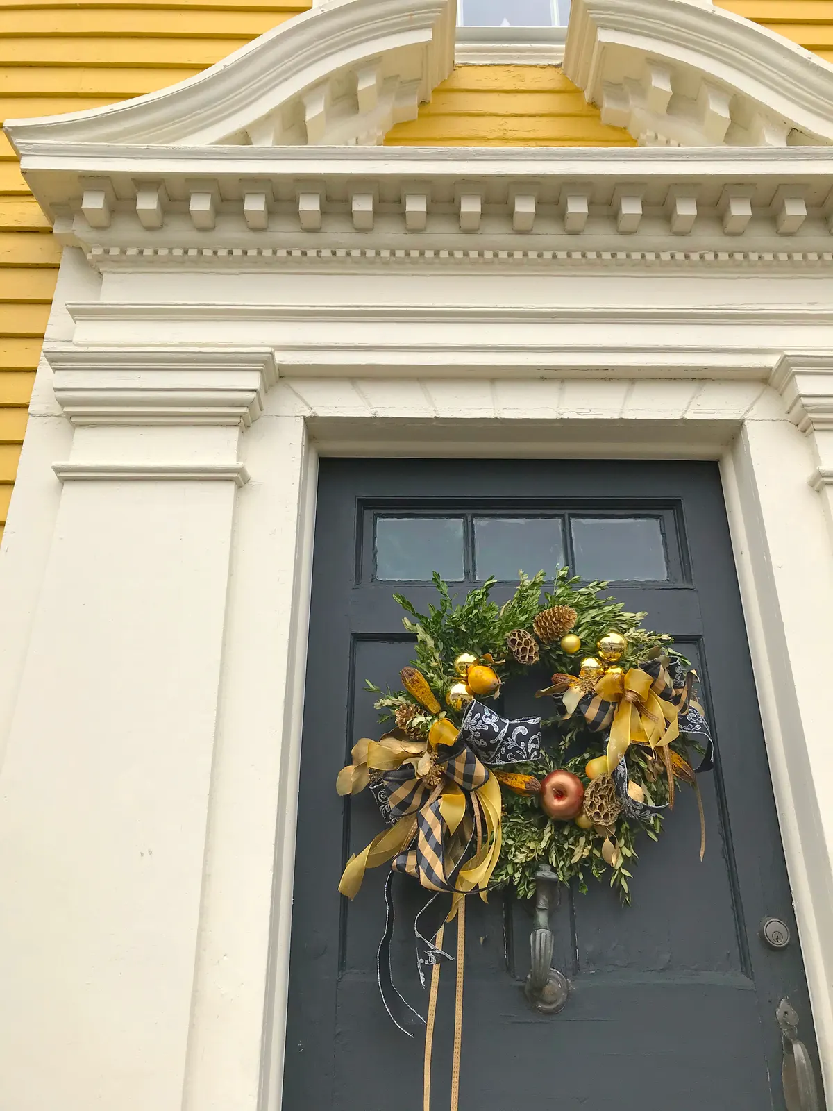 Charcoal gray front door with a greenery wreath, pinecones, gold and copper ornaments and black and white ribbon
