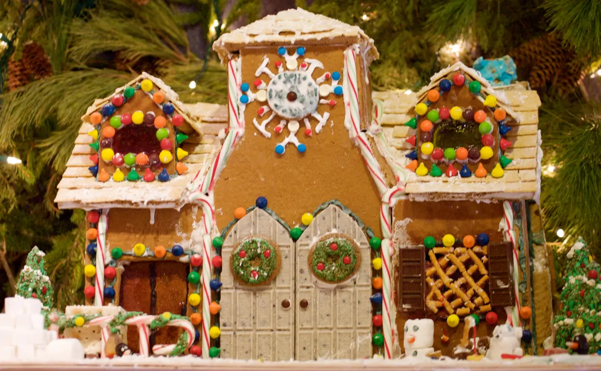Gingerbread house with white double doors, wreaths, candy canes, gumdrops and a pretzel lattice window