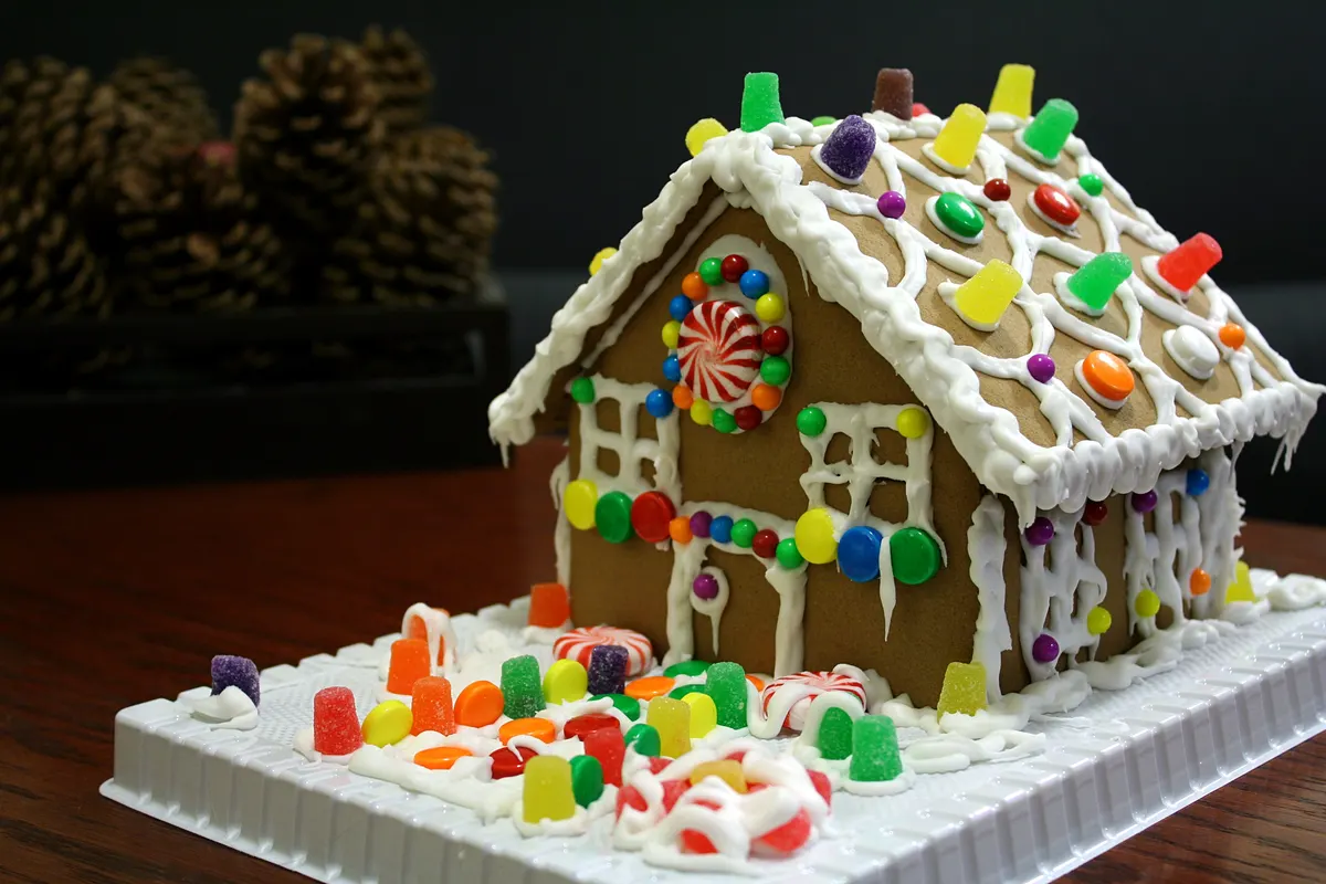 Gingerbread house with white icing trim covered in colorful gumdrops, round candies and peppermint swirls