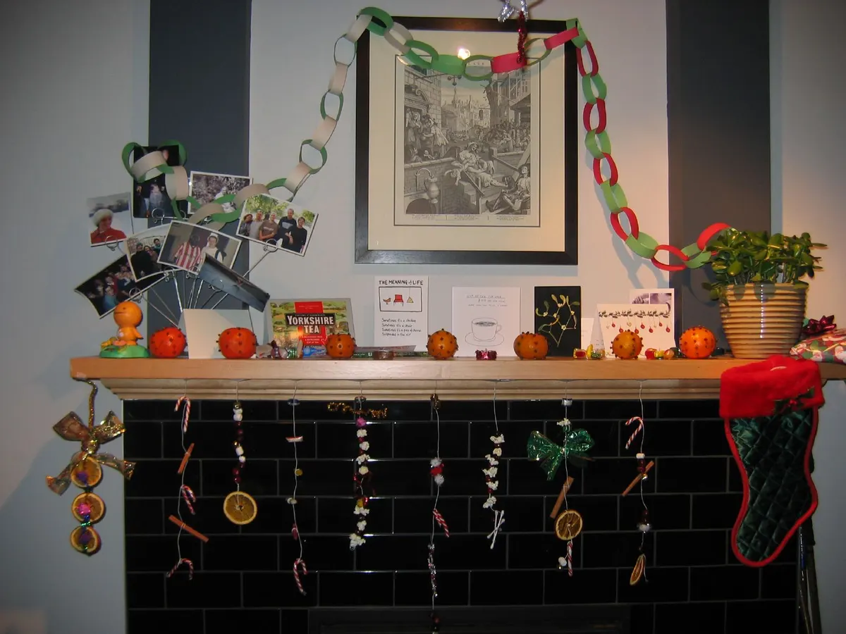 Light wood mantel with clove-studded oranges, greeting cards and a dried orange slice garland hanging over black tiles