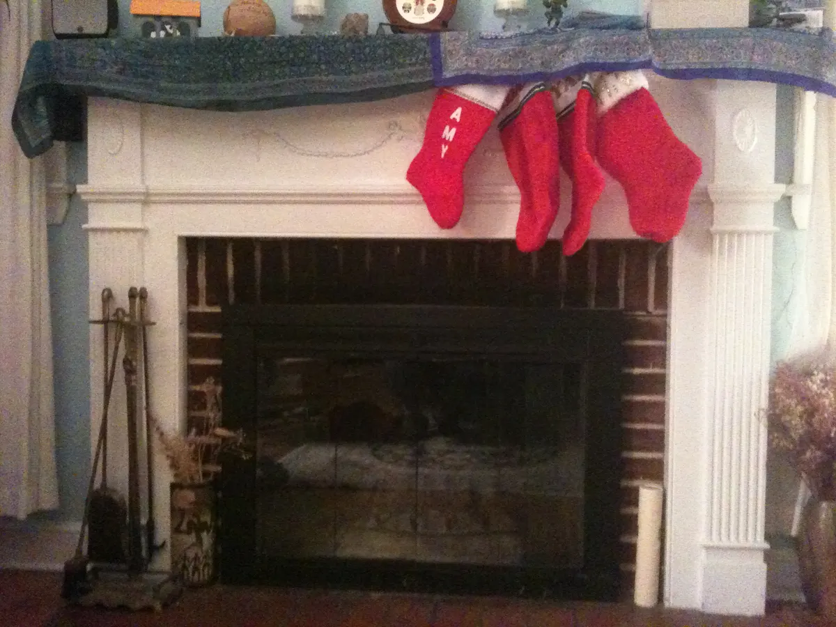 White painted fireplace with a teal patterned runner draped over the mantel and four red stockings hanging from it