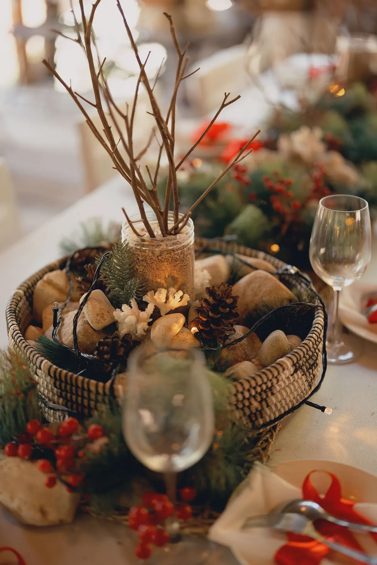 Woven basket of pinecones, stones and evergreen on an ivory table with a berry garland and warm string lights