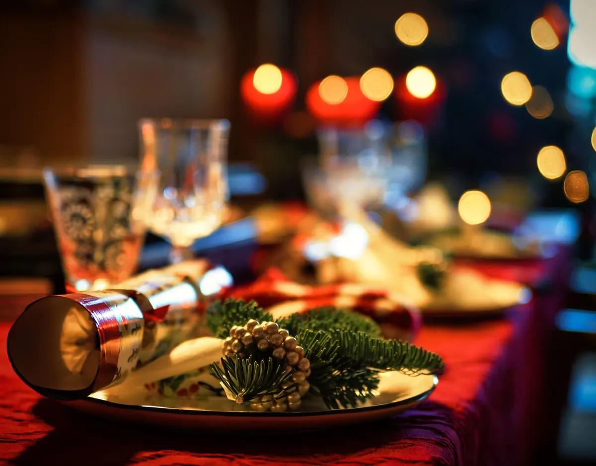 Cream rolled napkin with a fir sprig and gold beaded ring beside a gold Christmas cracker on red cloth