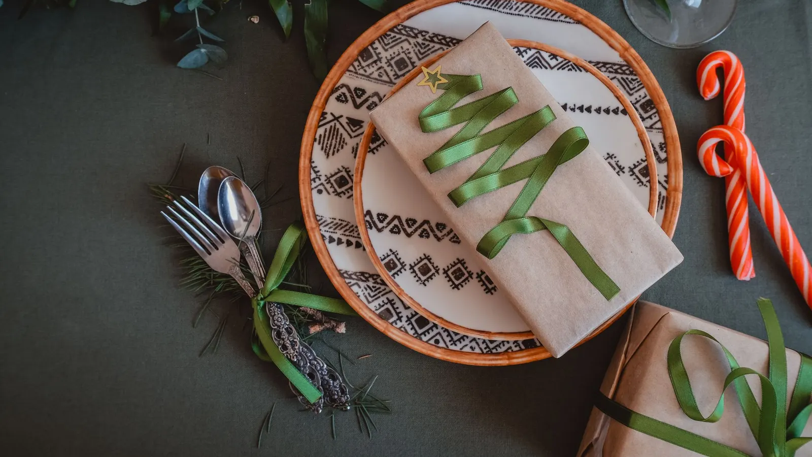 Dark green tablecloth with a white plate, beige napkin shaped like a tree with green ribbon and candy canes