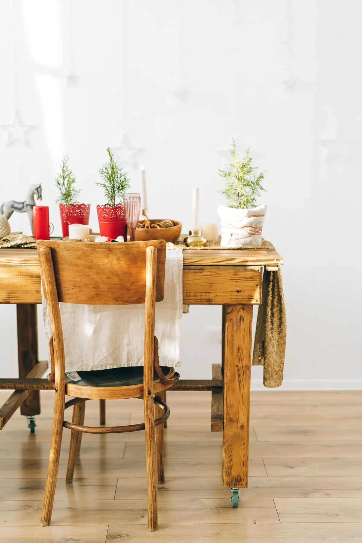 Wooden table with a gold sequin runner, three small potted evergreens, a bowl of dried citrus and candles