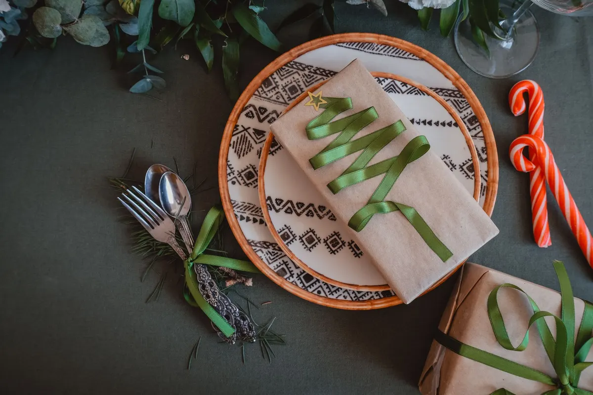 Dark green tablecloth with a white plate, beige napkin shaped like a tree with green ribbon and candy canes