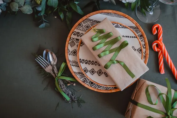 Dark green tablecloth with a white plate, beige napkin shaped like a tree with green ribbon and candy canes