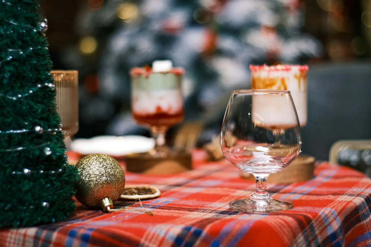 Red tartan tablecloth with a small green tree wrapped in silver beads, a gold bauble and a clear goblet