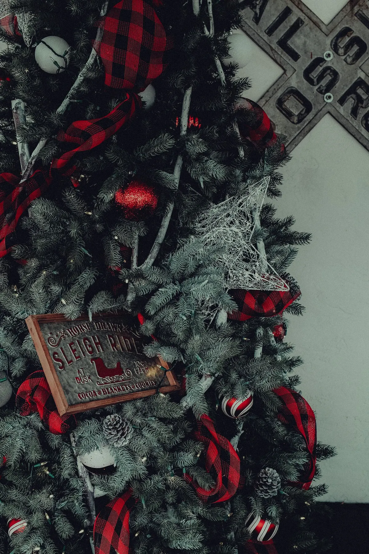 Flocked tree with red and white balls, snowy pinecones, a white star and red and black buffalo-check ribbon