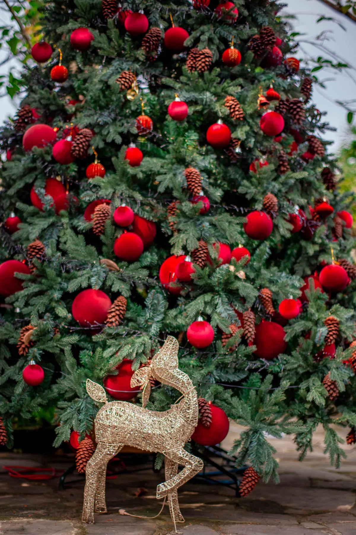 Green tree with red balls in several sizes, pinecones and a small gold bell, with a glittery gold reindeer at its base