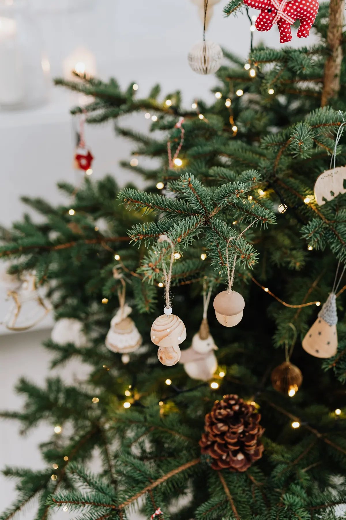 Green tree with wooden mushroom, acorn, pinecone and bell ornaments in cream and tan under warm white lights