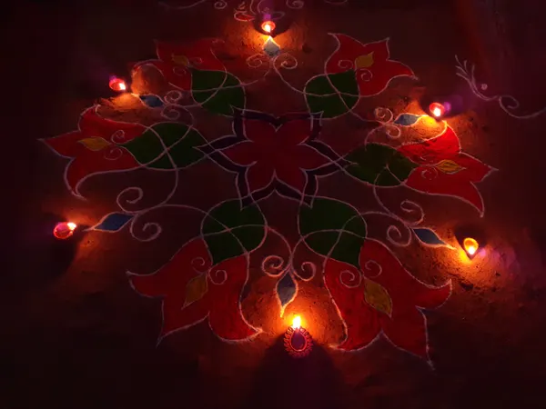 Floral rangoli in red, green and white on the floor, surrounded by small lit clay diyas