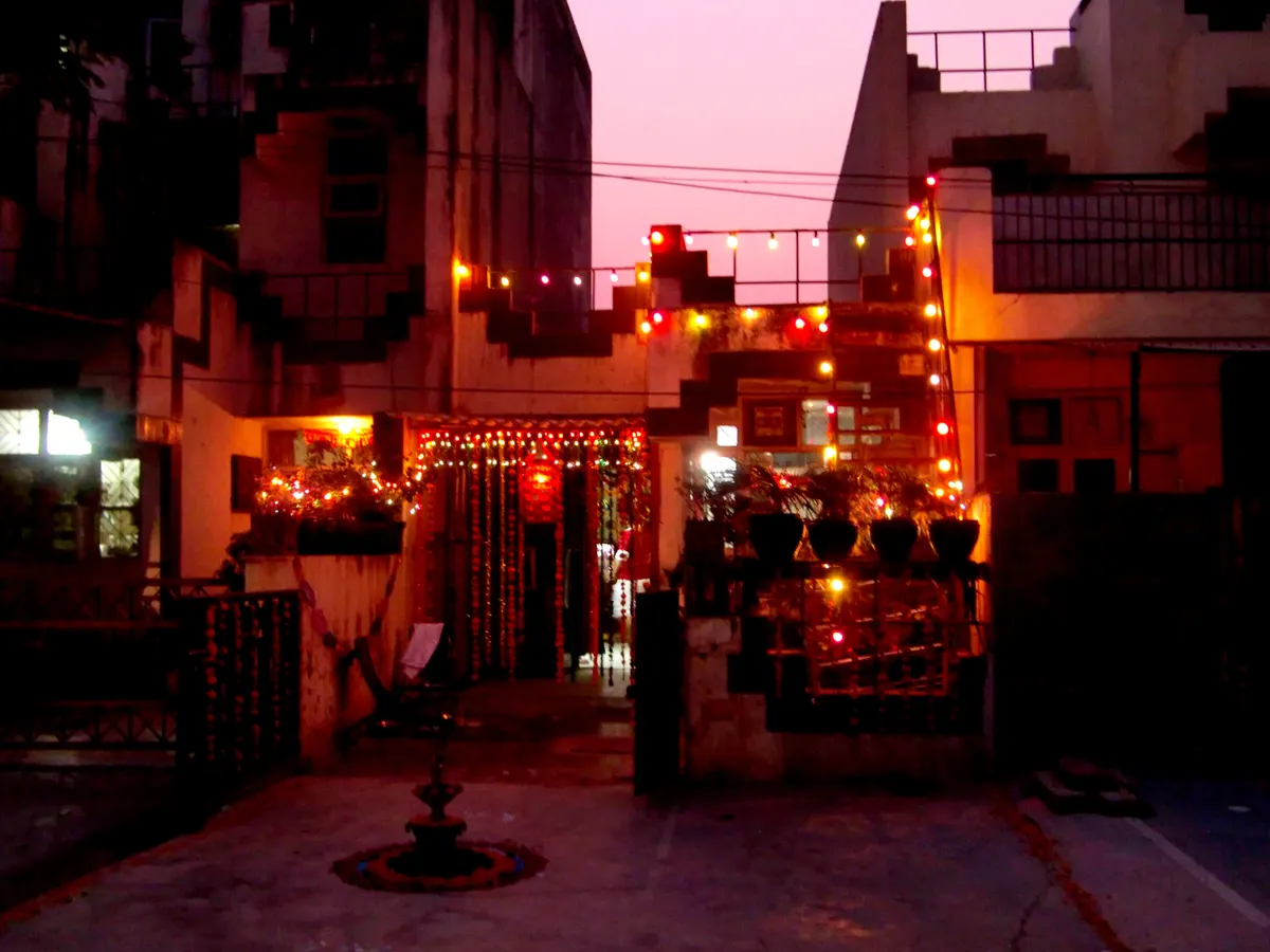 House front at dusk covered in red and orange string lights, with a gate and courtyard