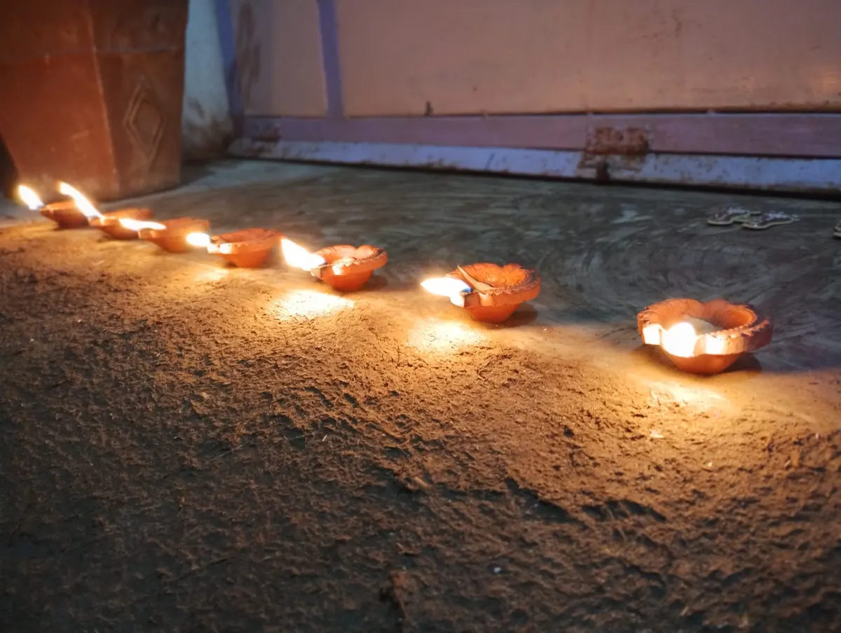 Row of lit clay diyas lined up along a rough concrete ledge at dusk