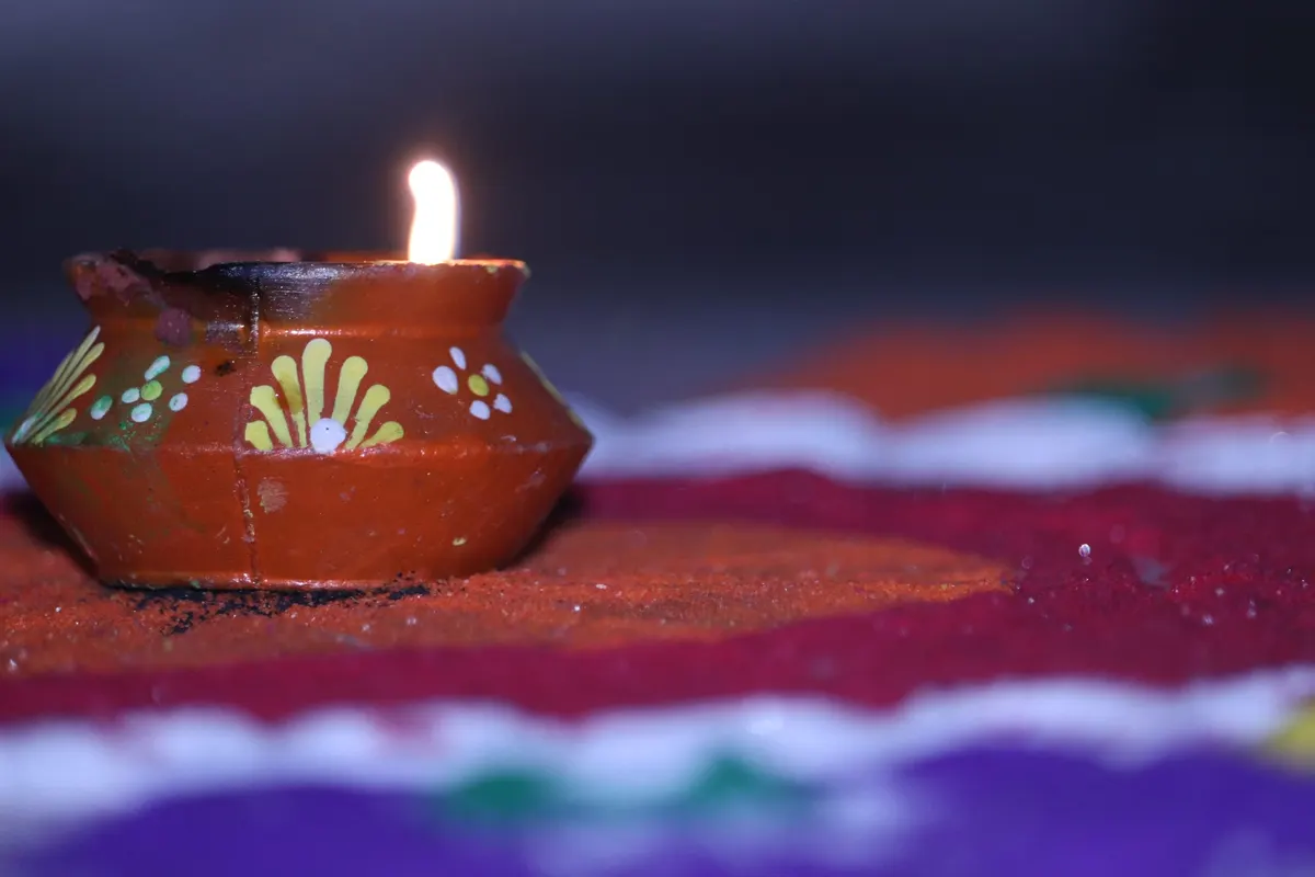 Close-up of a lit terracotta diya with painted patterns resting on a colorful rangoli