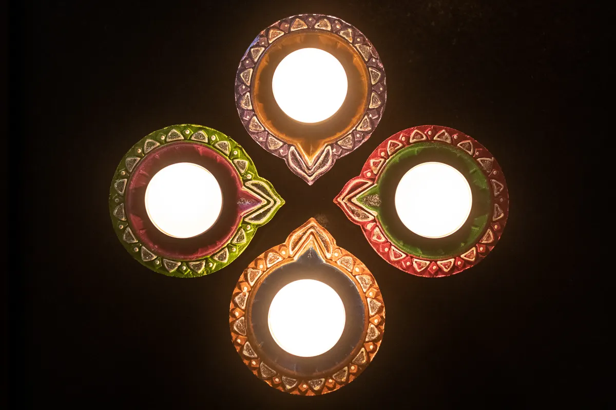 Four painted clay diyas arranged in a cross and glowing against a black background