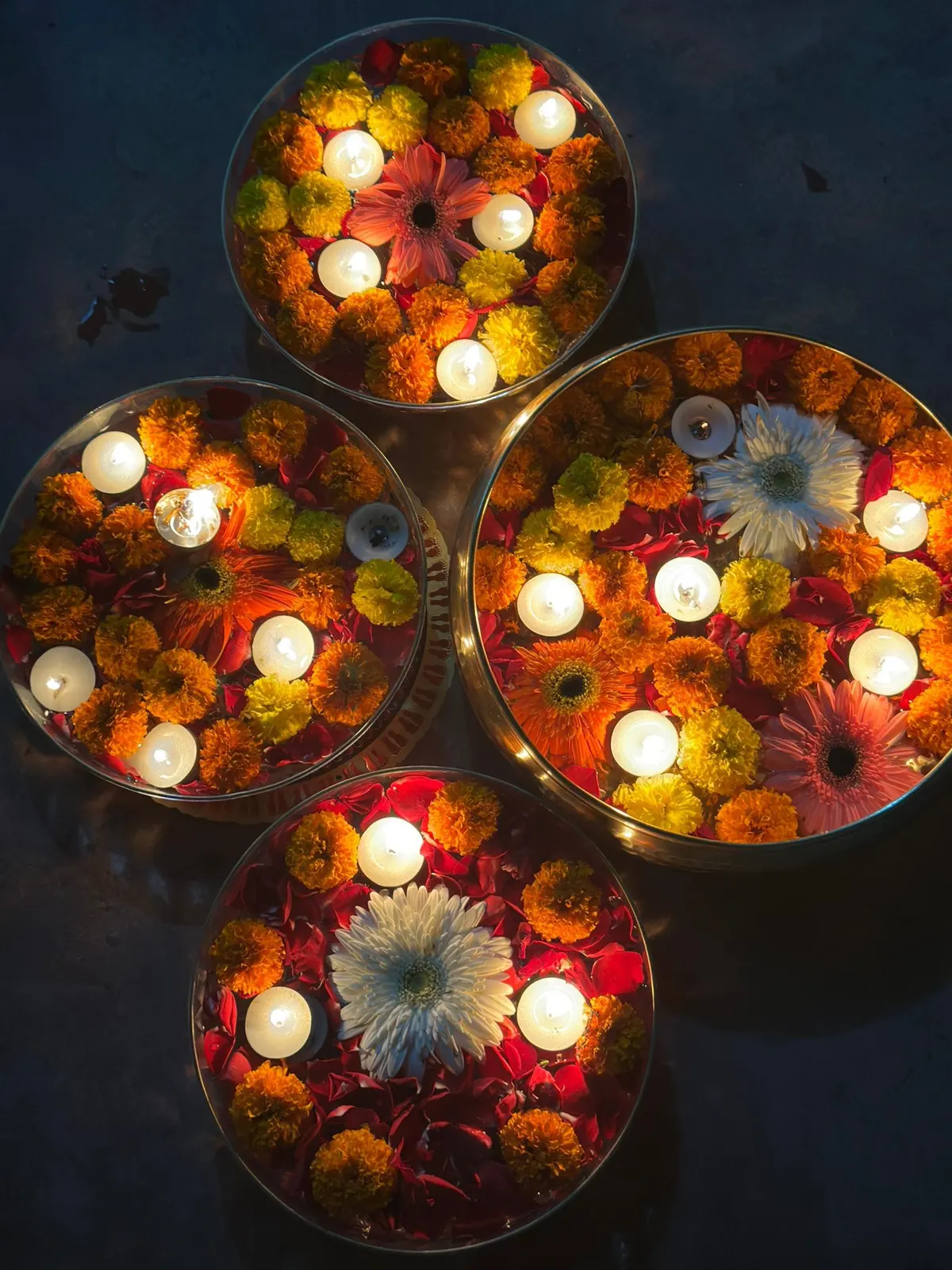 Overhead view of round trays filled with marigold and gerbera petals and floating candles