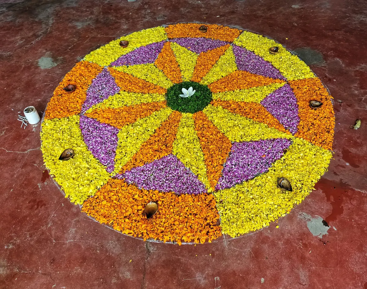 Large circular flower rangoli in yellow, orange and purple petals with small diyas around the edge