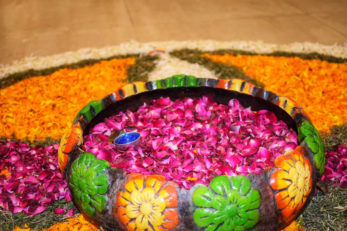 Bowl of pink rose petals set on a flower rangoli made of marigolds and loose petals