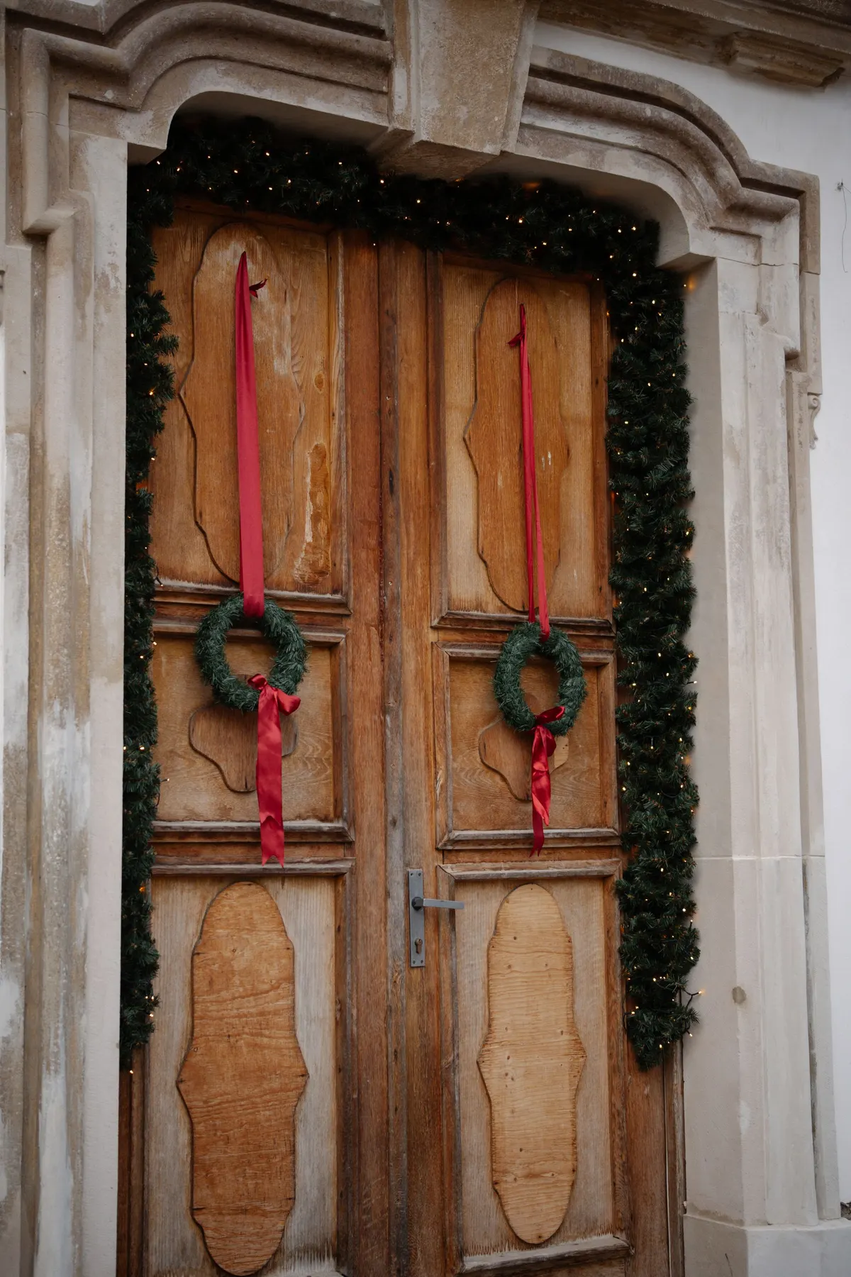 Brown wooden double door in a gray stone frame with a green wreath and red ribbon on each leaf