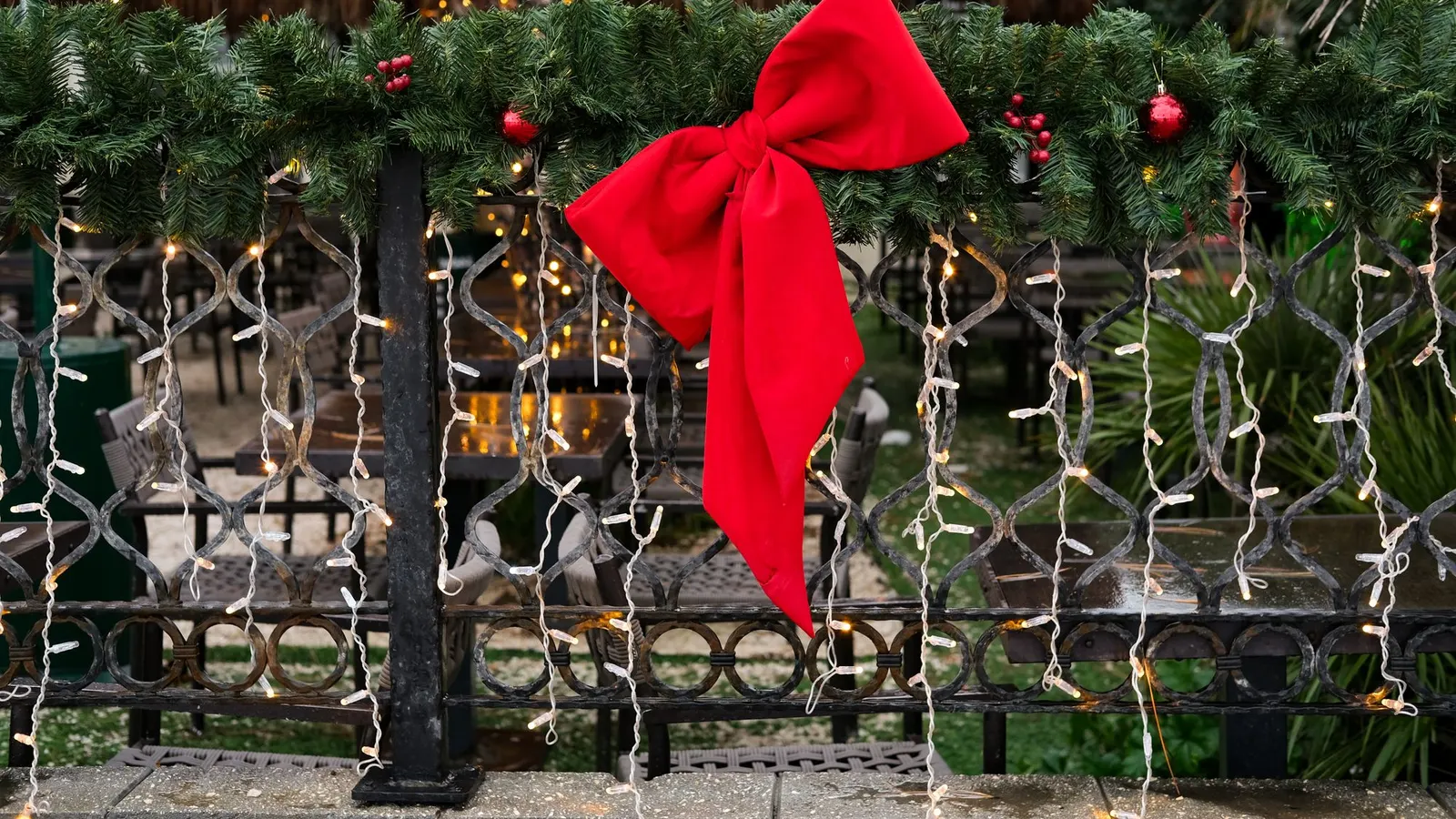 Black metal railing draped with green garland, a large red bow, red ornaments and warm string lights