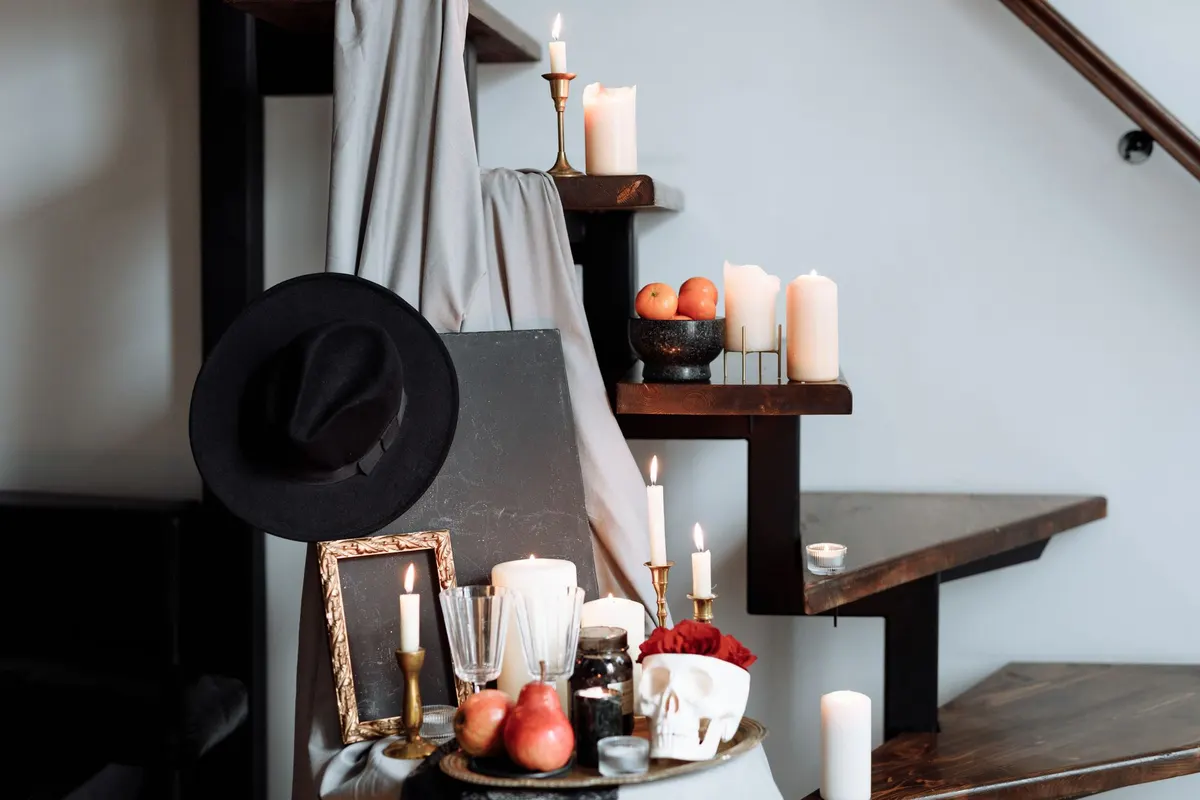 Dark wood stairs with white tapers in brass holders, a white skull planter of red roses and a black hat
