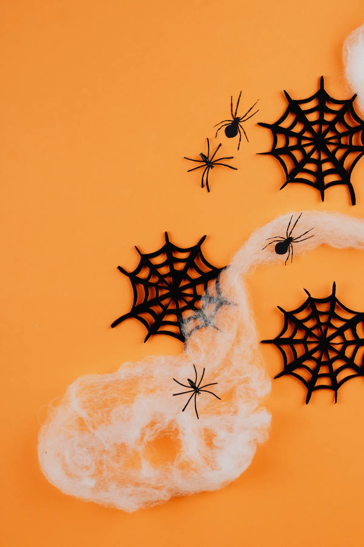 Three black spiderweb cutouts, four plastic spiders and white stretch cobweb on a bright orange surface