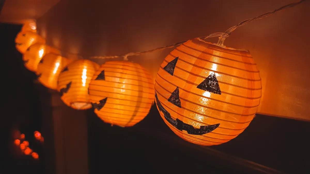 String of glowing round orange lanterns with black jack-o'-lantern faces on a white wire in a dark room
