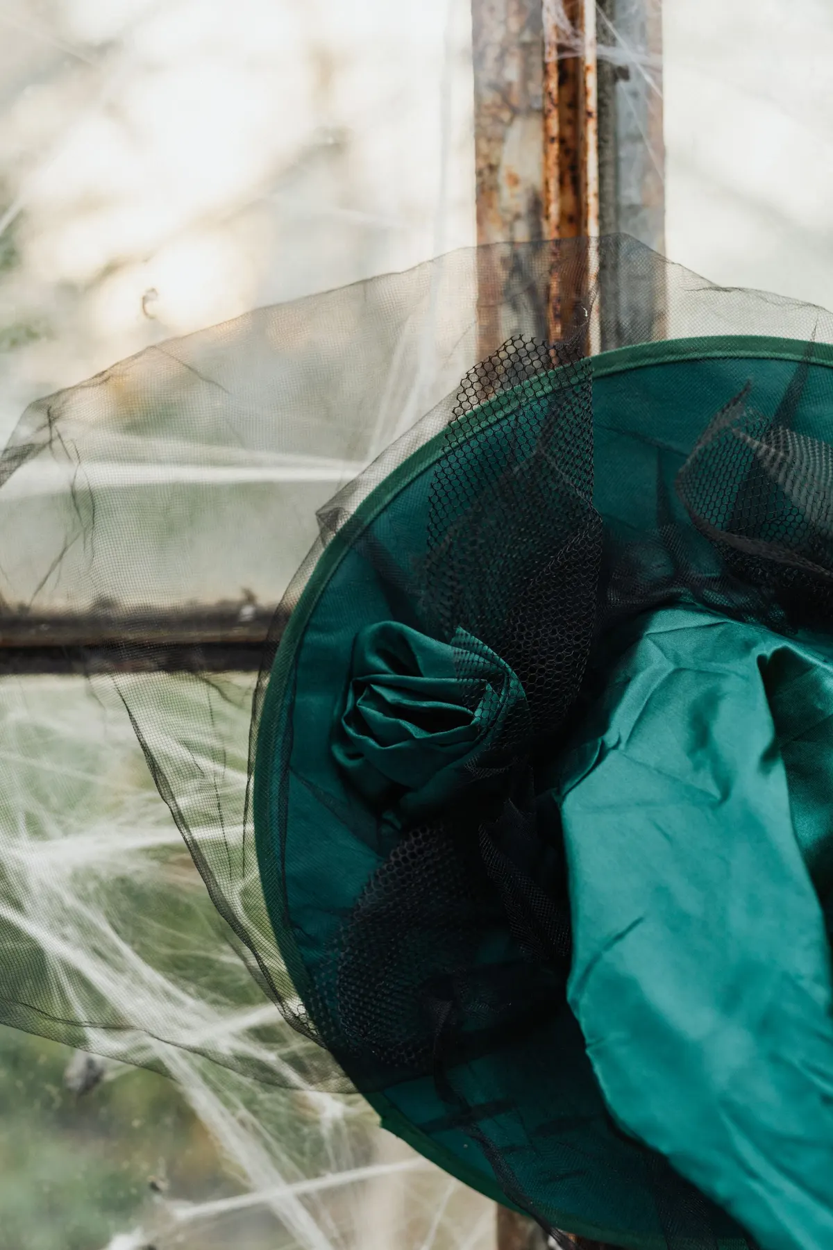 Emerald satin witch hat with a satin rosette, black netting and a long tulle veil on a cobwebbed window