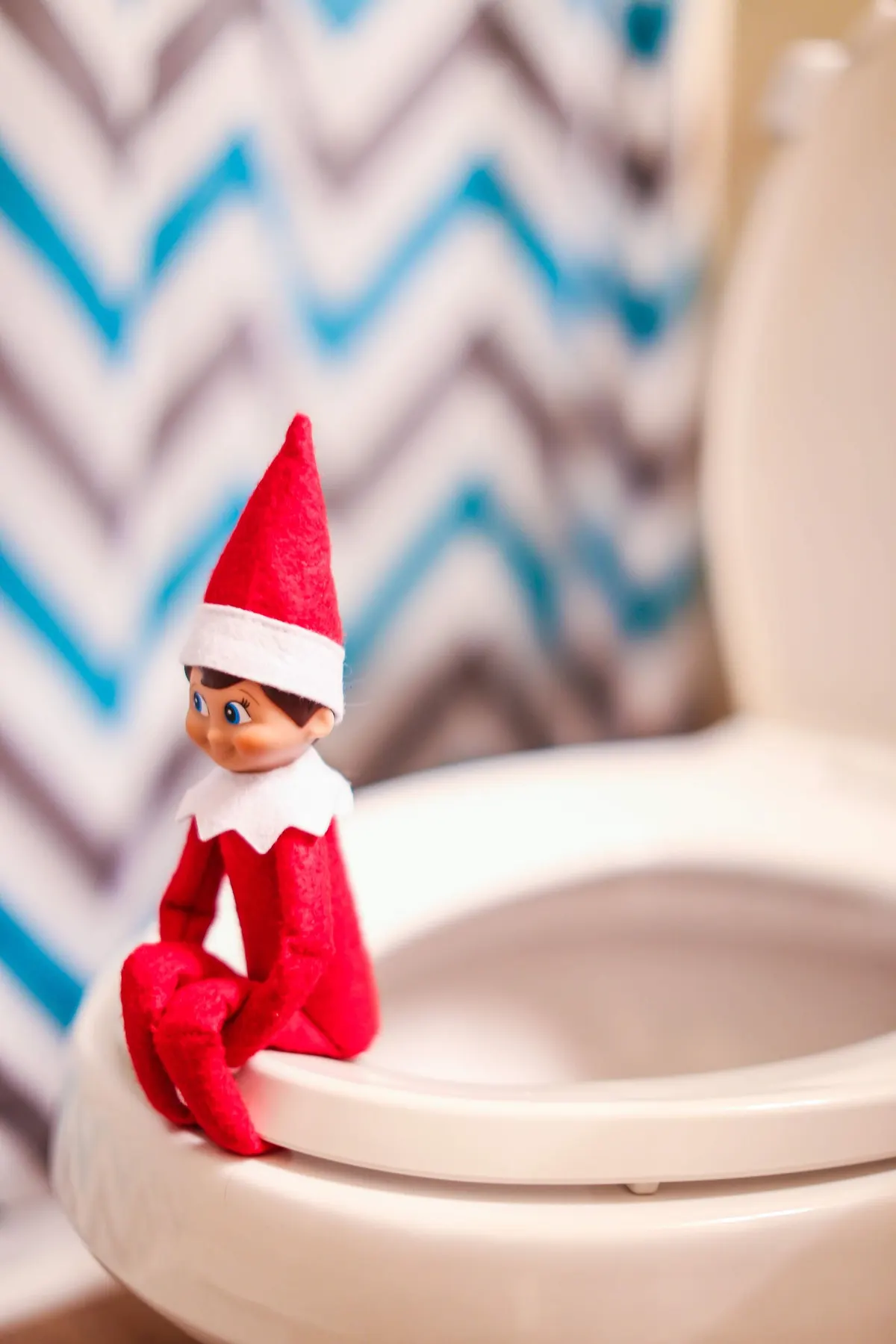 Small red elf doll with a tall red and white hat perched on the edge of a toilet seat