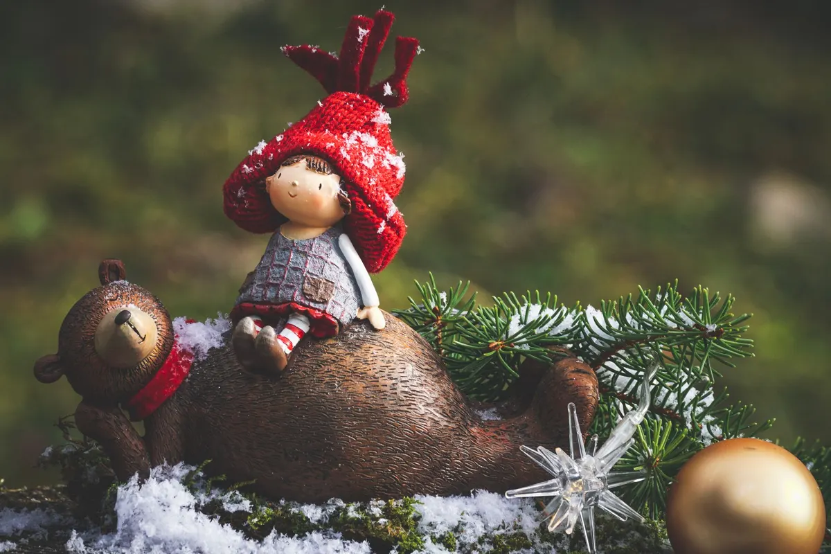 Elf figure in a red knit hat and striped stockings riding a brown toy bear on fake snow