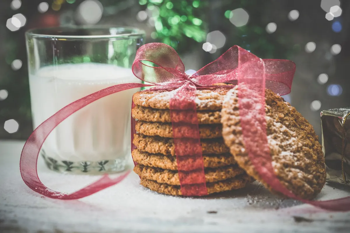 Stack of about seven cookies tied with red ribbon beside a glass of milk and a wrapped gift