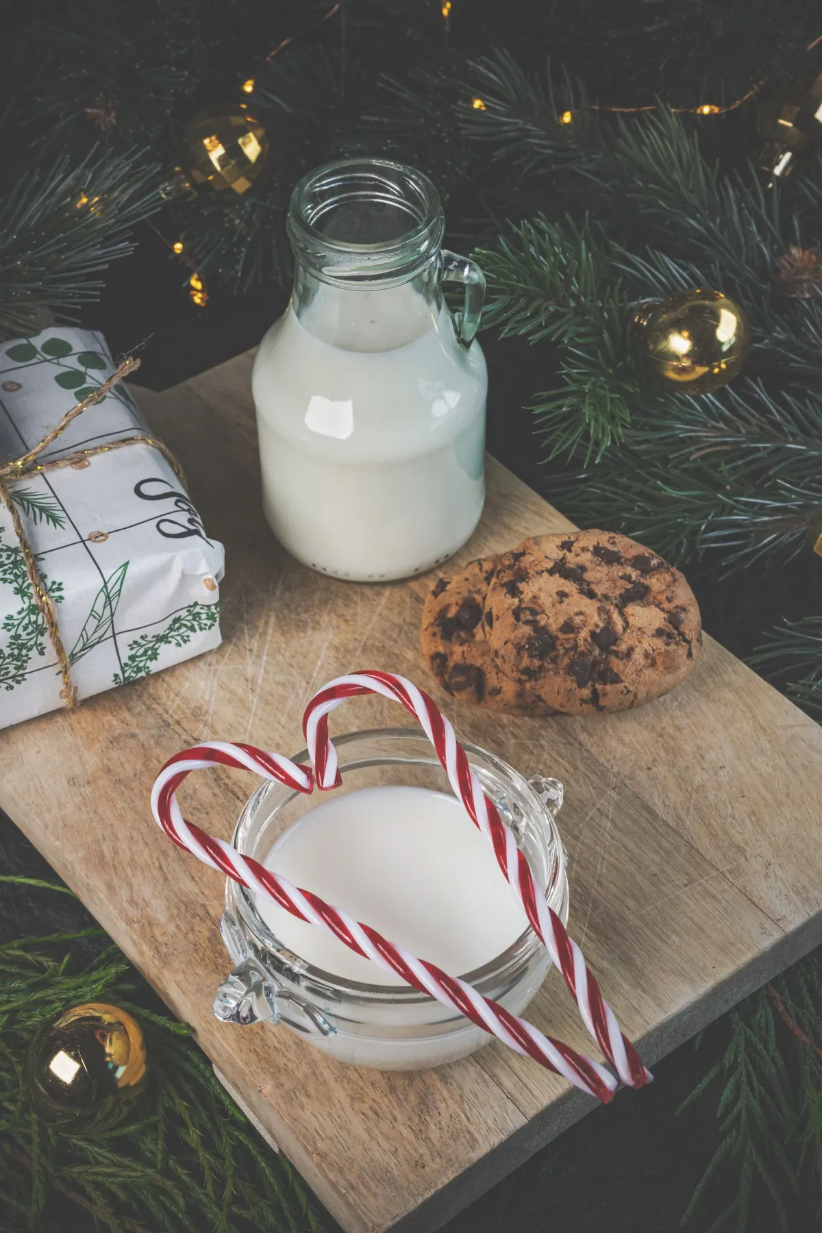Wooden board with a milk bottle, a milk jar, two candy canes, two cookies and a wrapped gift