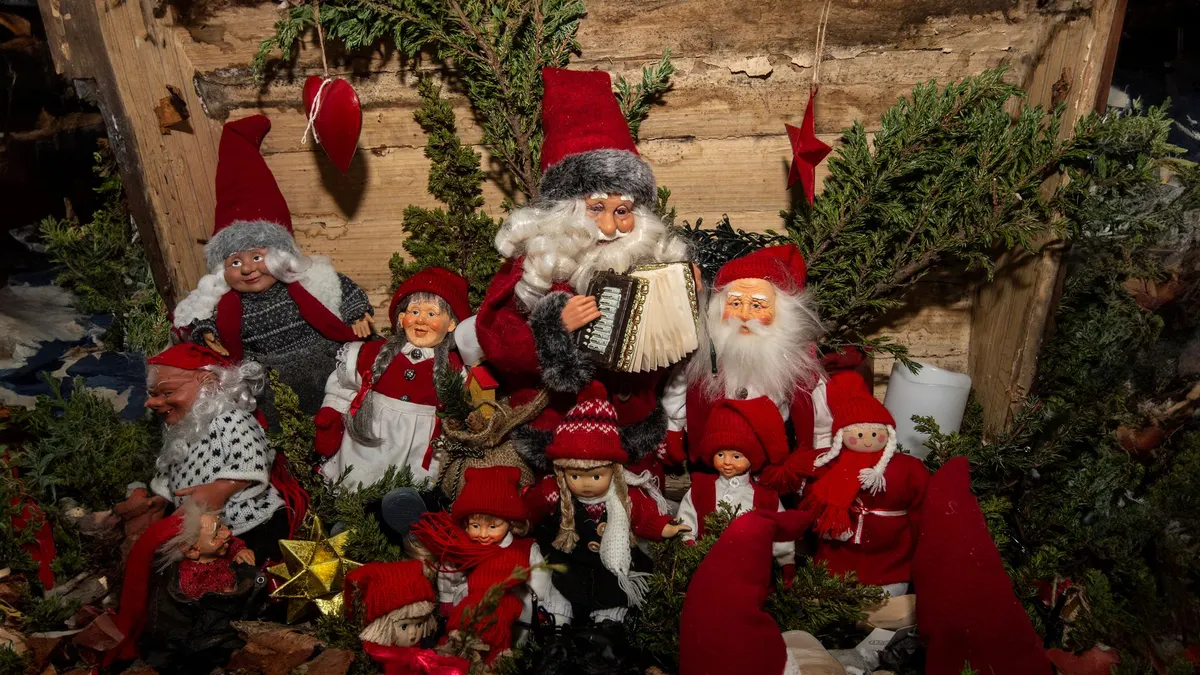 About a dozen elf and Santa figures with red hats gathered in greenery around one playing an accordion