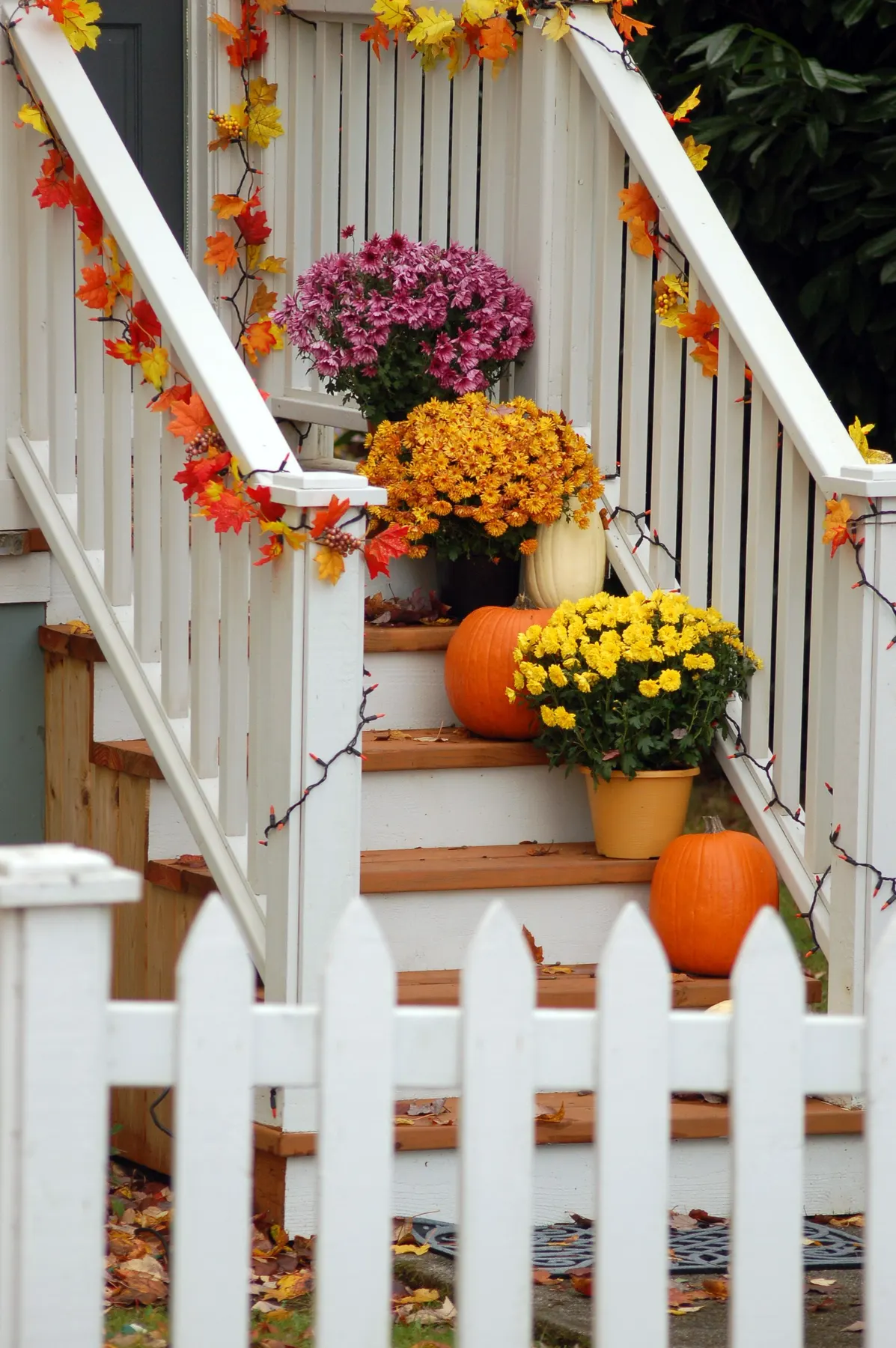 White-railed porch stairs with pink and yellow mums, pumpkins and orange leaf garlands on the steps
