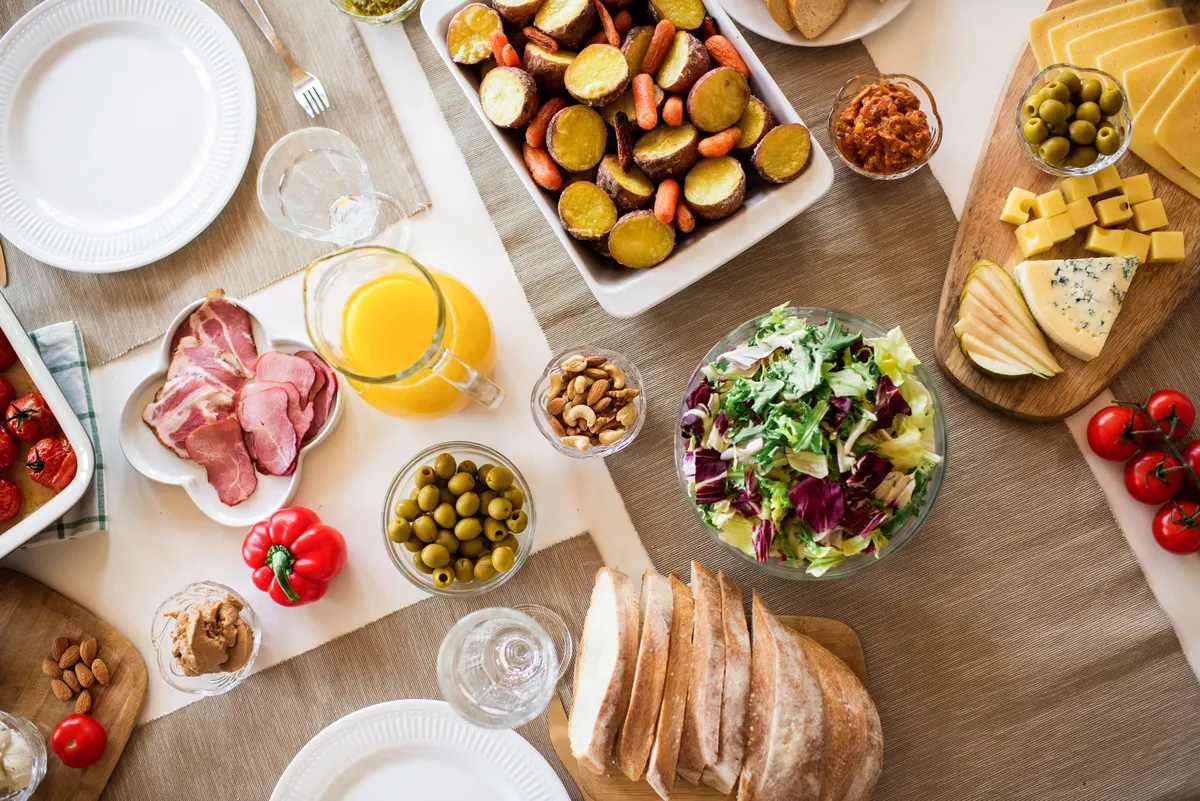 Buffet table with a roast vegetable platter, meat dish, salad bowl, juice pitcher and wooden boards