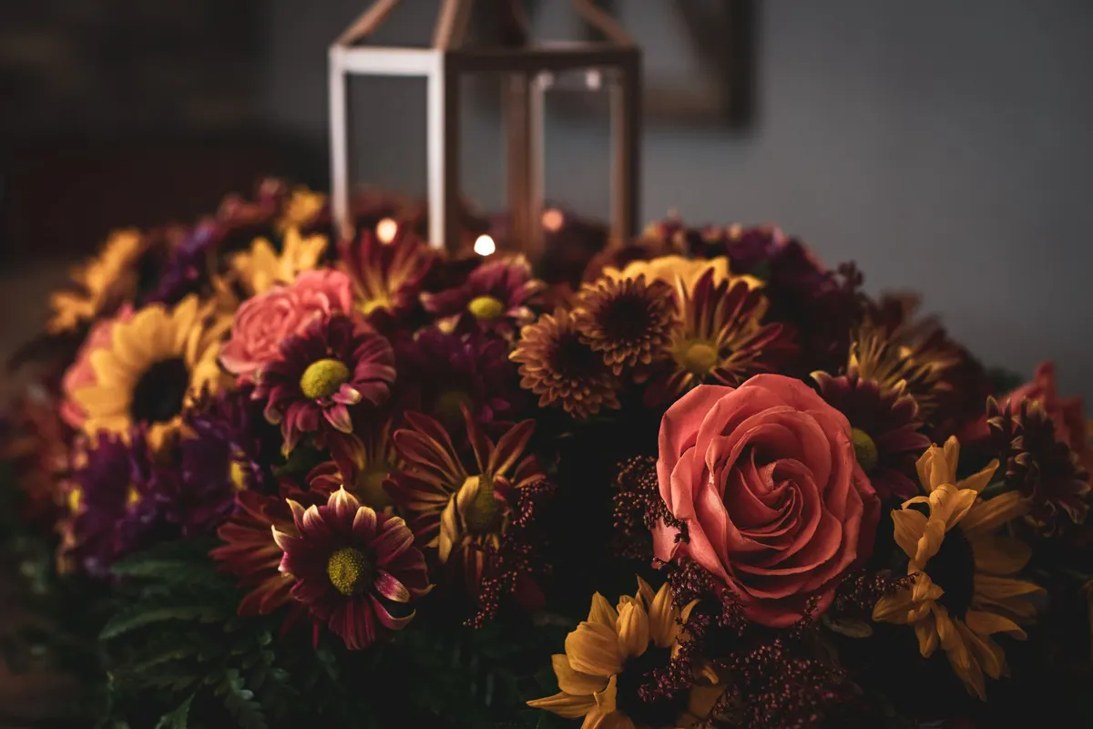 Bronze metal and glass lantern surrounded by coral roses, sunflowers and burgundy chrysanthemums