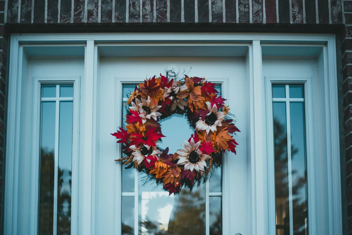Fall wreath of cream flowers and rust fabric leaves hanging on a white door with dark brick surround