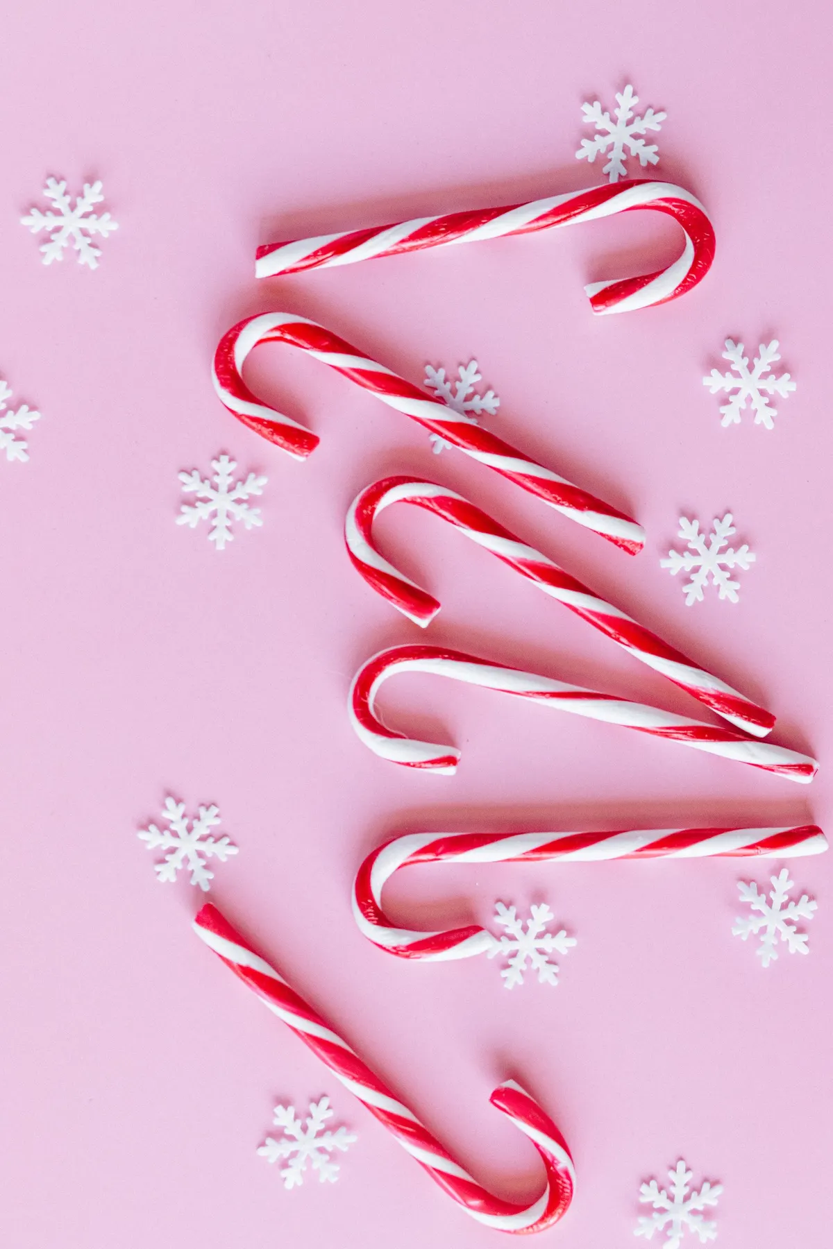 Six red and white striped candy canes and white snowflake decorations on a pink background