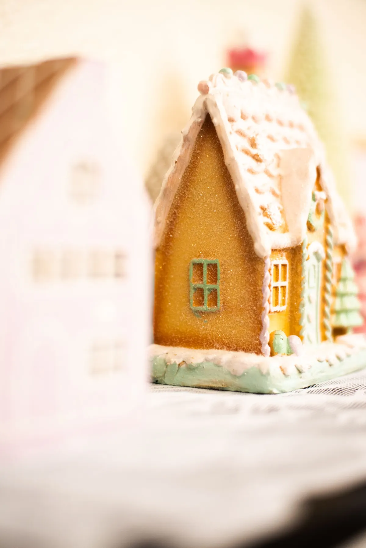 Golden-brown gingerbread house with white icing, green window trim and pastel candies on a pale green base