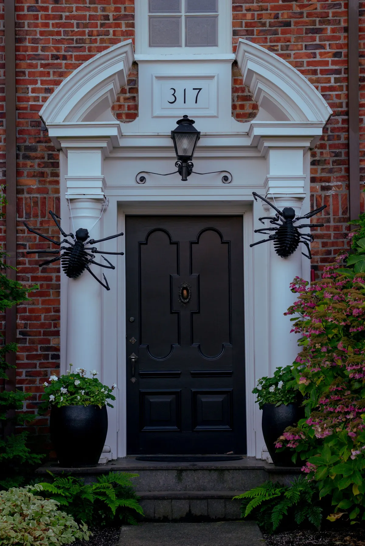 Red brick house with a white columned doorway, a black door and two large black spiders on the columns
