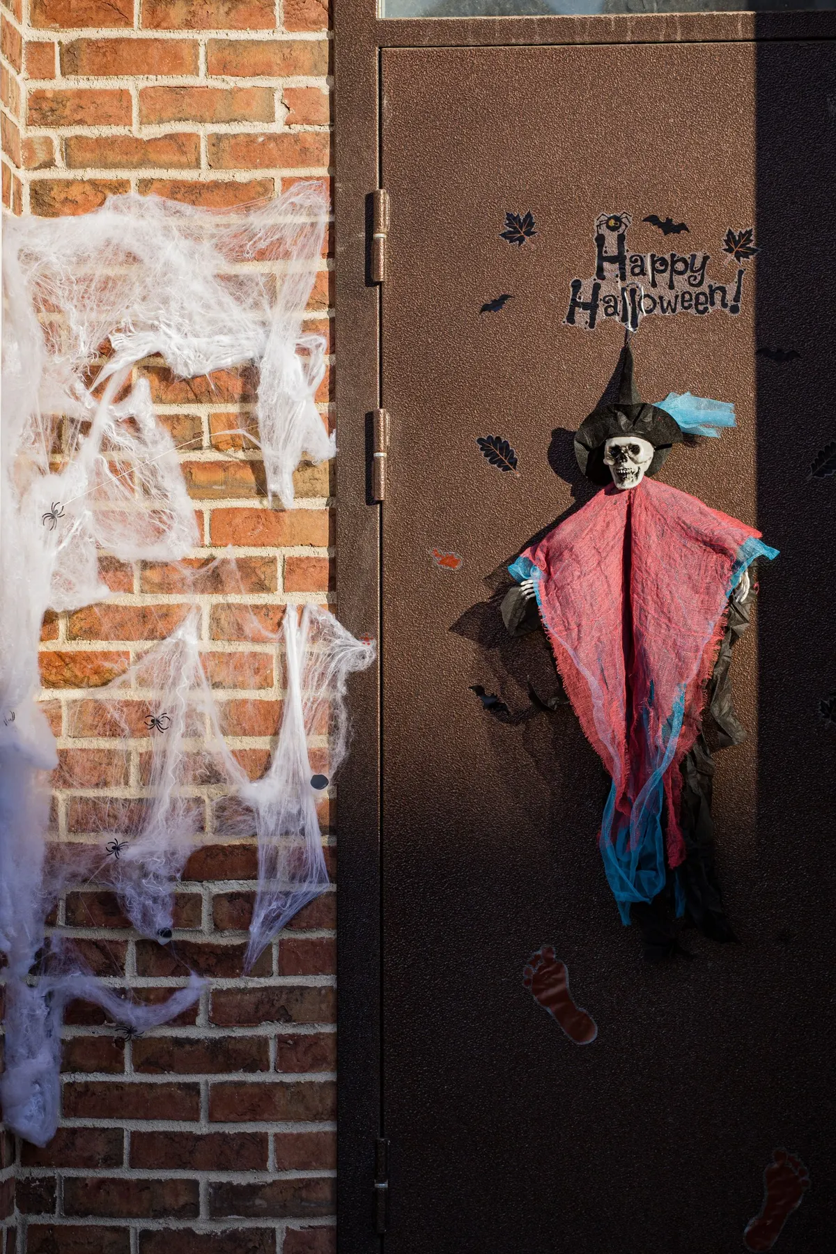 Dark brown door with a Happy Halloween decal, black bat and leaf stickers and a hanging skeleton in a witch hat
