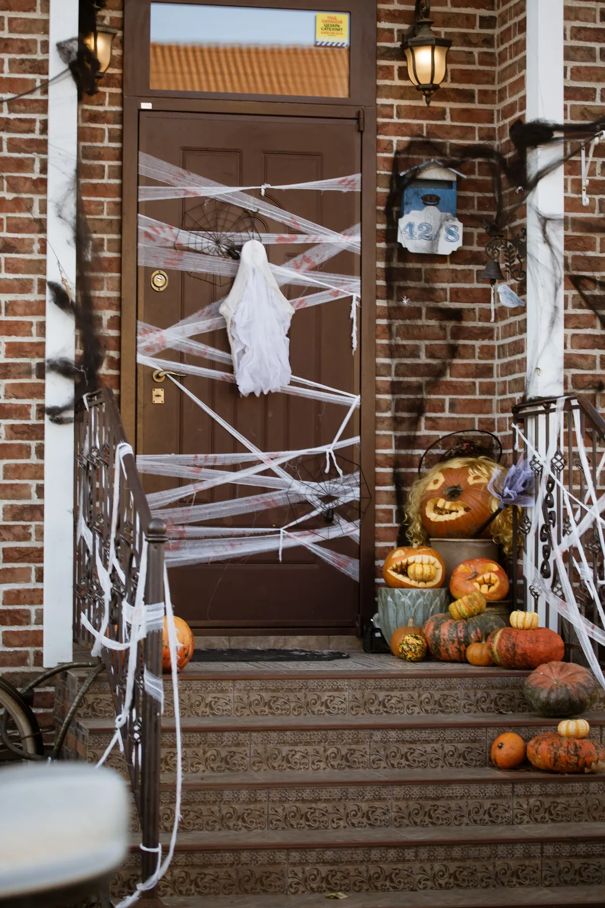 Brown door crisscrossed with white gauze strands and a faceless cheesecloth ghost, black webbing on the railings