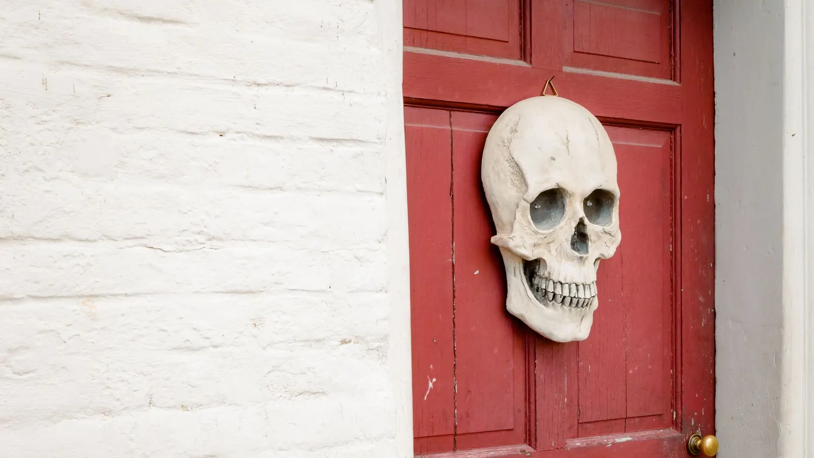 Red panelled door against white-painted brick with one large bone-white plastic skull hanging from a small hook