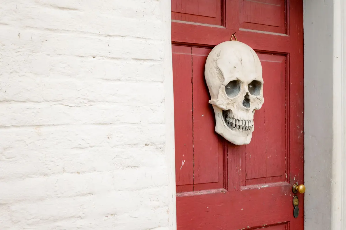 Red panelled door against white-painted brick with one large bone-white plastic skull hanging from a small hook