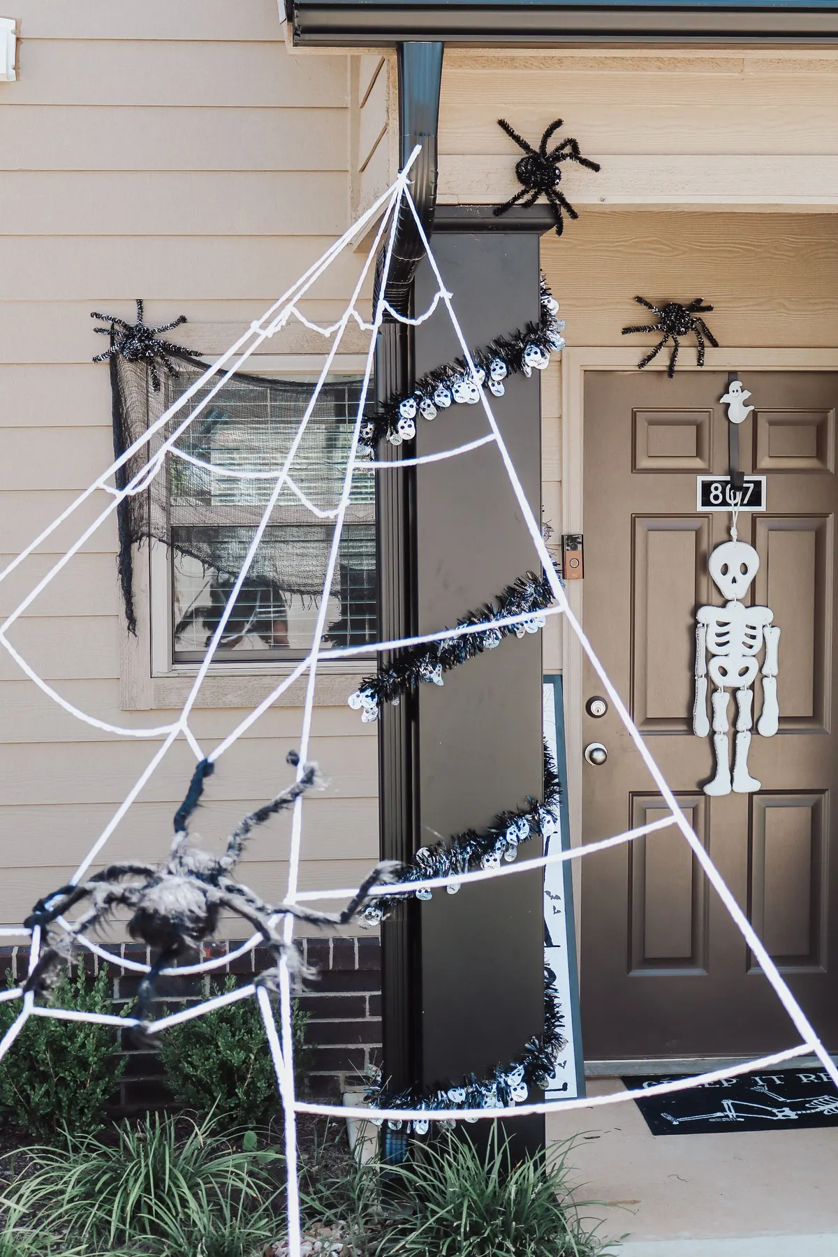 Porch with a large white rope spiderweb, a furry black spider at its base and a skeleton cutout on the door