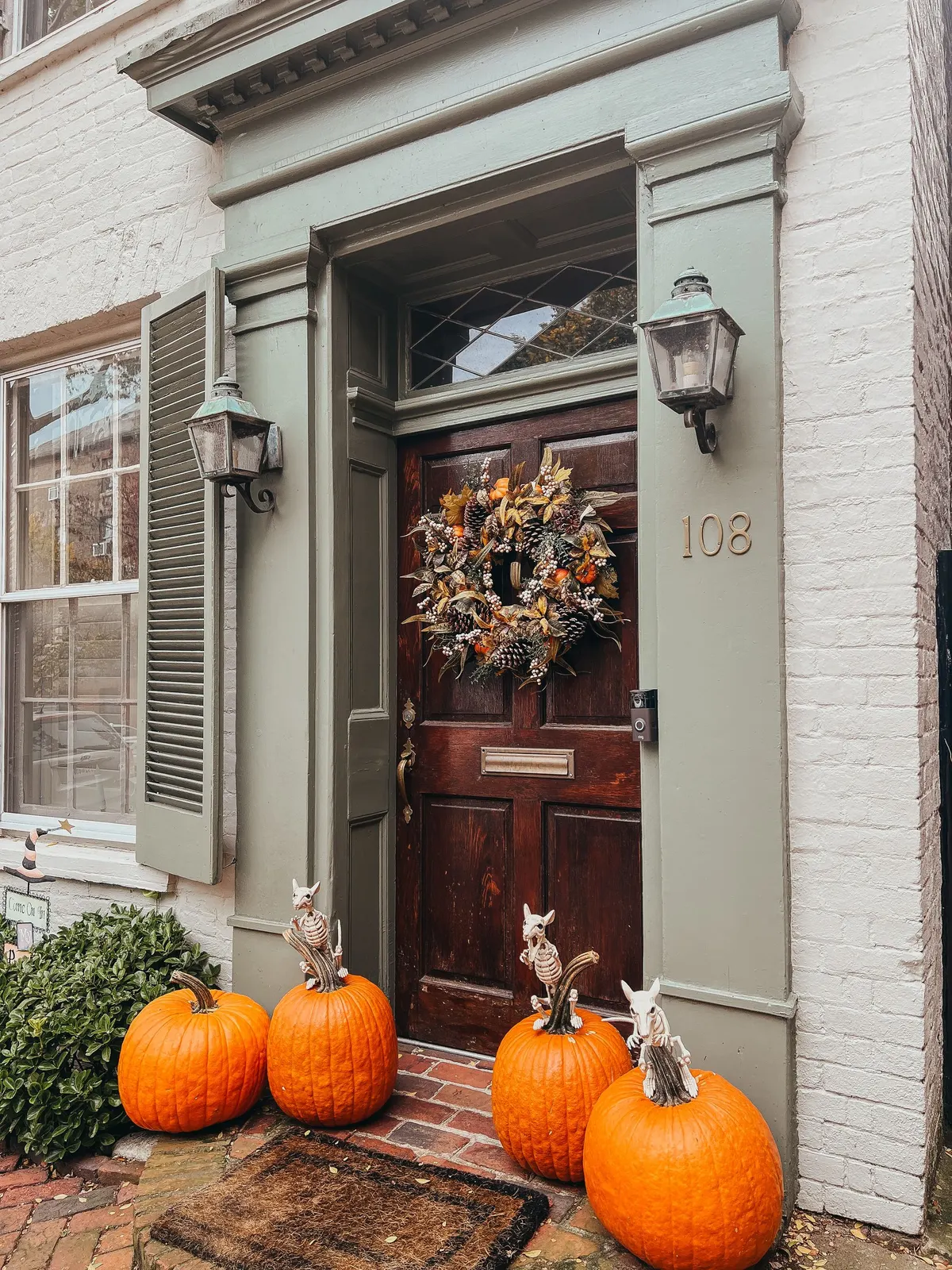 Dark wood door with a fall leaf wreath and four orange pumpkins, three topped with small white skeleton animal figures